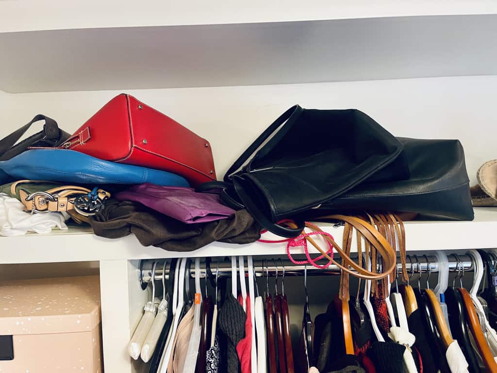 purses and handbags piled in a mess on the top shelf.
