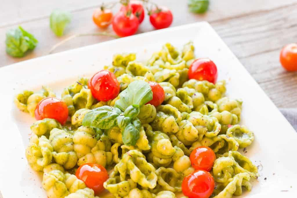 Pasta with pesto sauce basil and tomatoes on it.