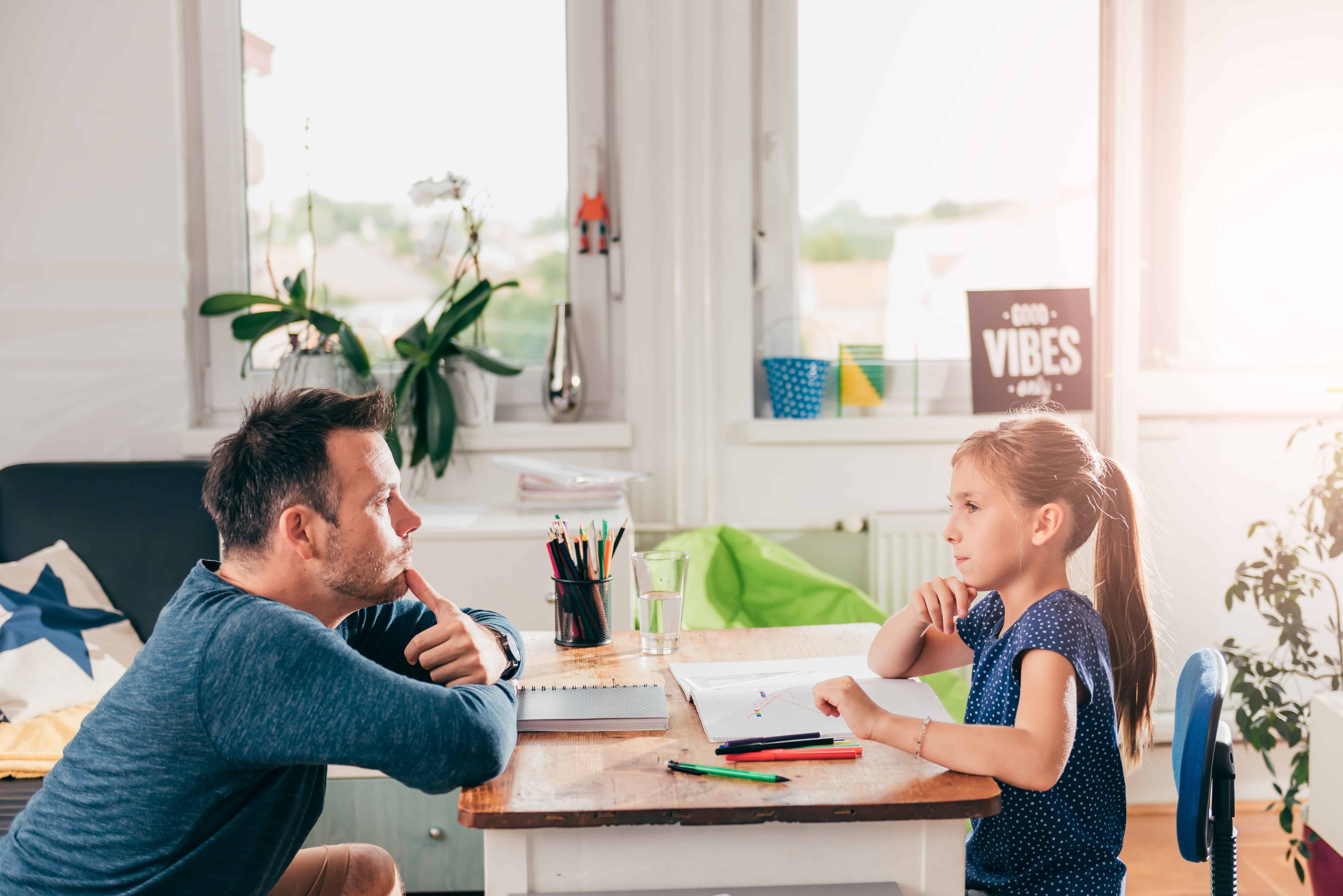 Dad siting at child size table across from his young daughter in a discussion.