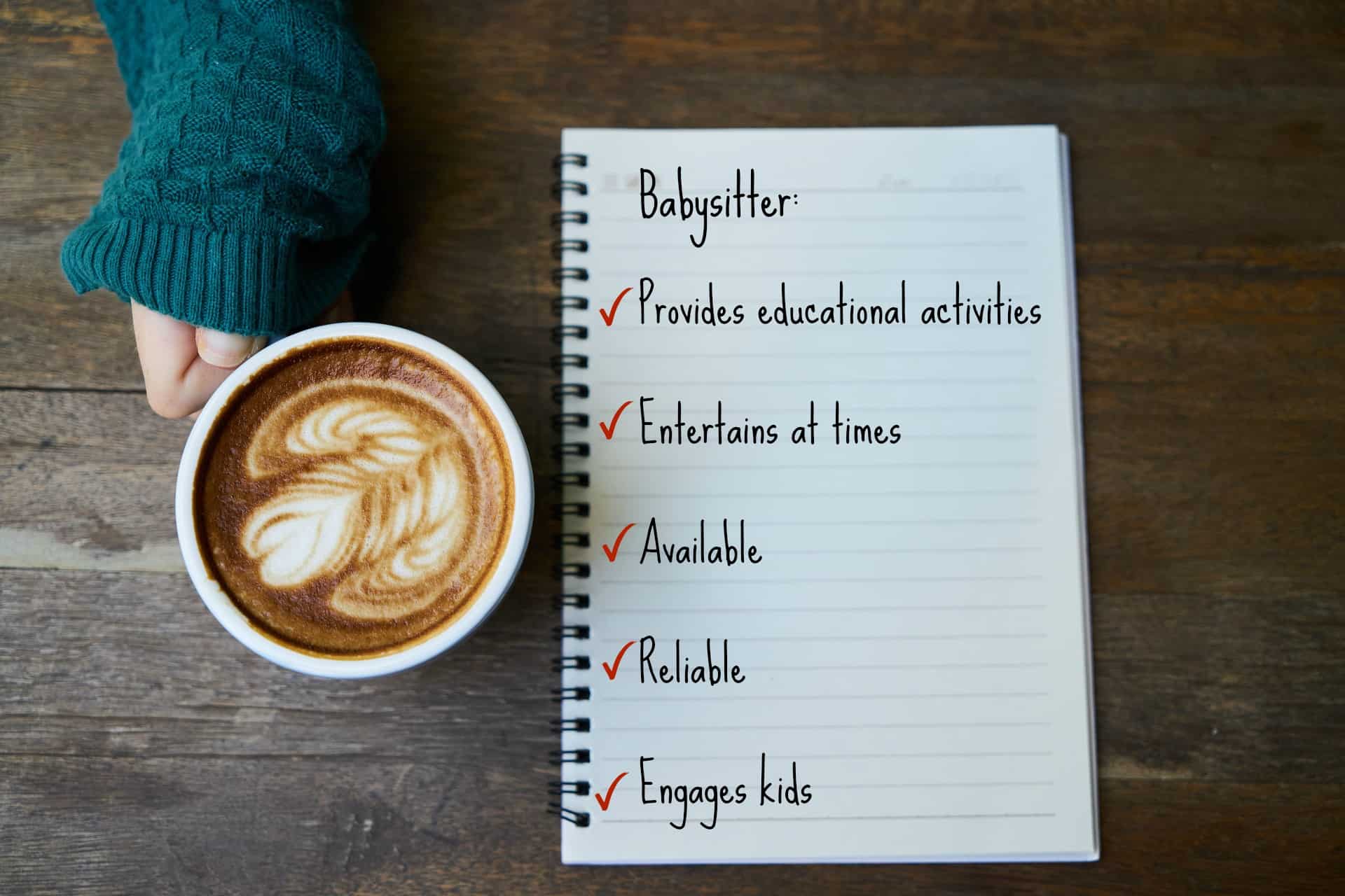 sweater sleeve covering hand holding a latte next to a notebook with Text = Babysitter, Provides educational activities, entertains at times, available, reliable, engages kids.