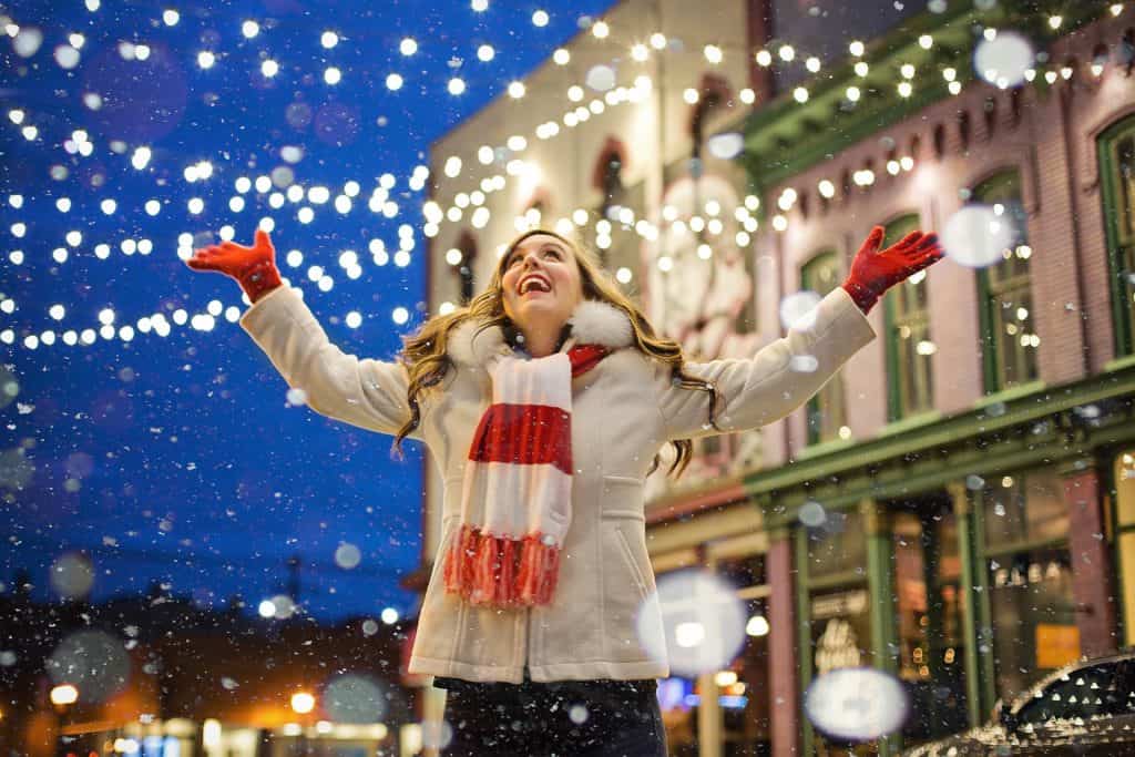 woman looking up at snow under christmas lights