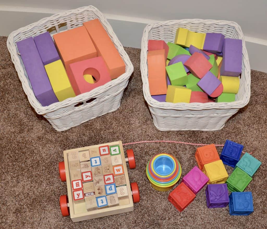 Bins with play foam blocks, building blocks and cups on the floor.