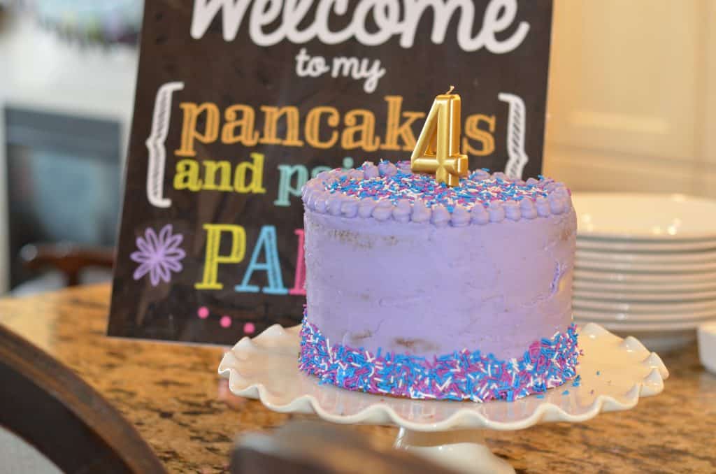 Purple birthday cake with a gold number four candle and birthday sign in the background