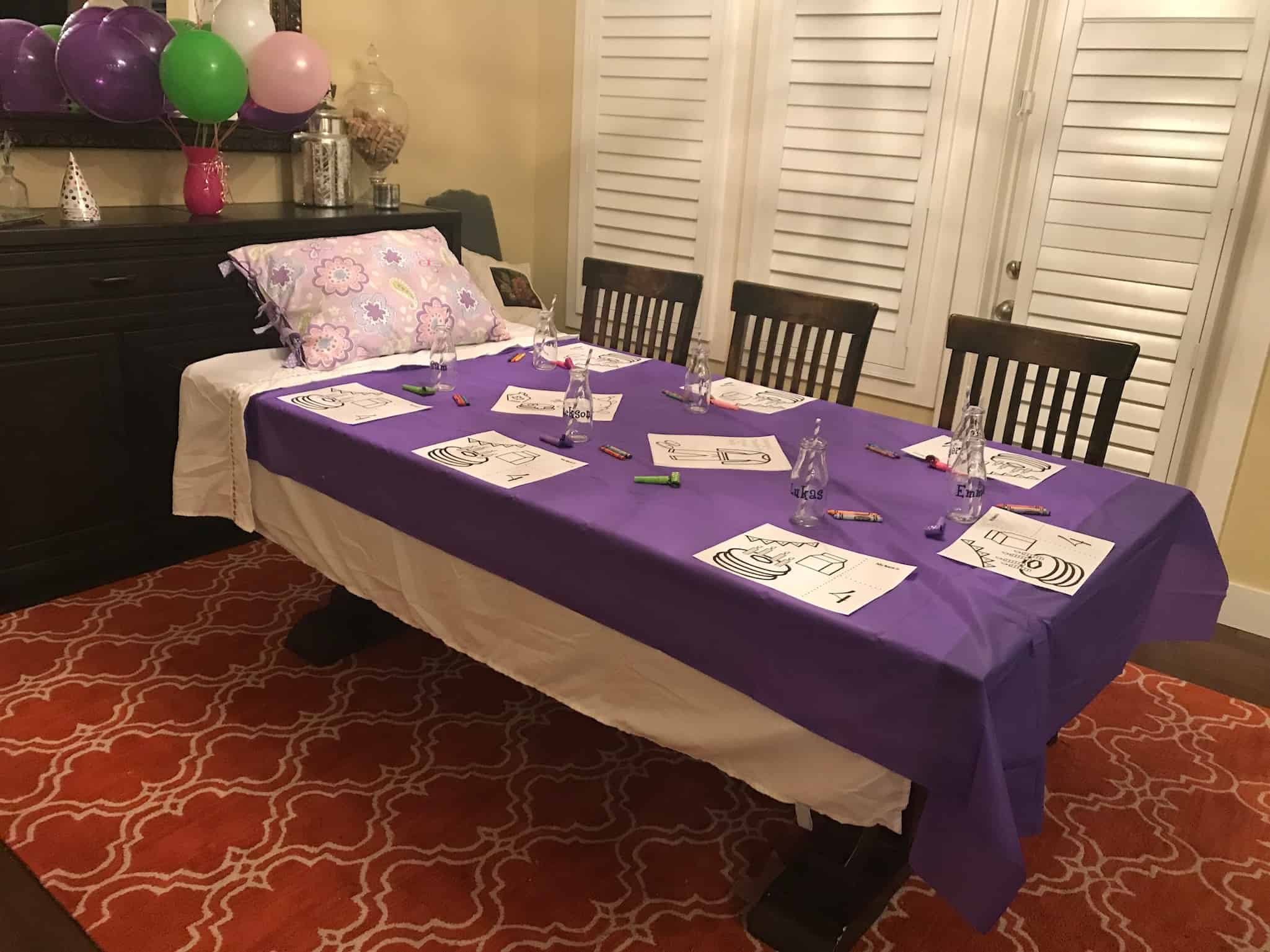 Dining room table covered with a twin bed sheet and plastic cover with a pillow at the head of the table to resemble a twin bed.