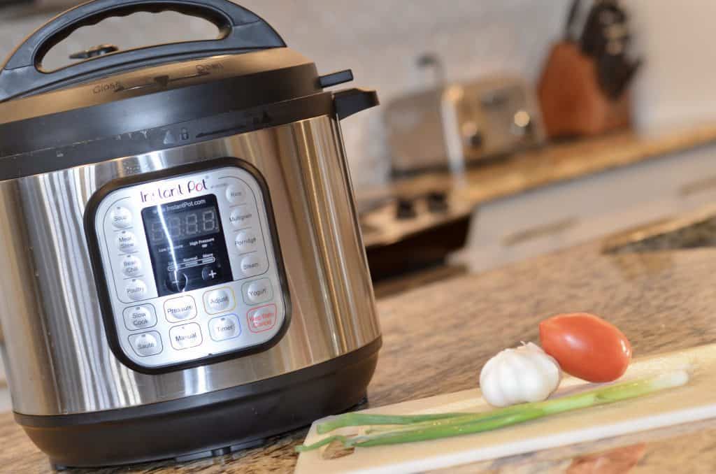 Instant Pot on a counter with a cutting board and vegetables on it.