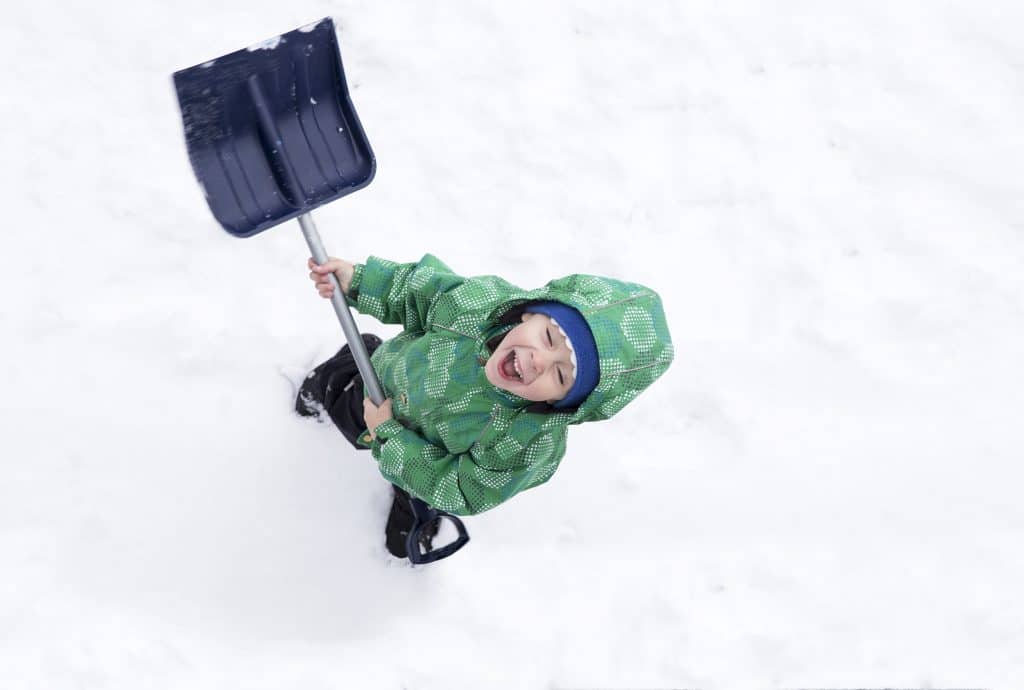 Preschool age boy showing enthusiasm while doing his chore of shoveling snow.