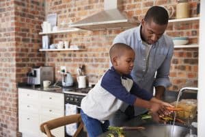 Father and son washing carrots at kitchen sink.