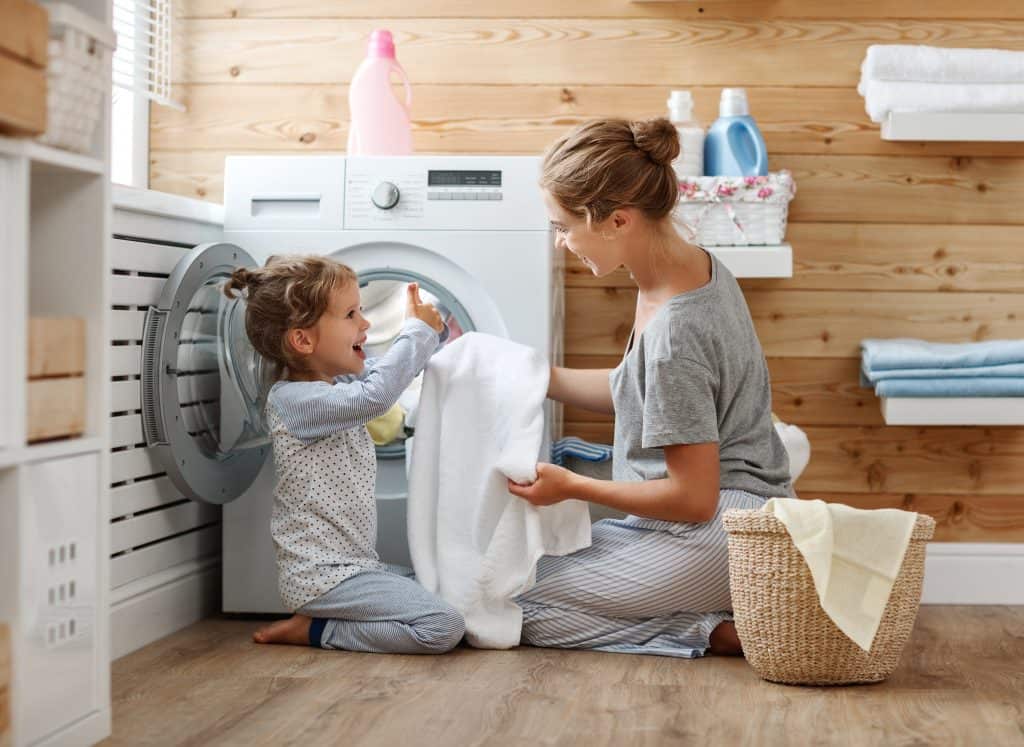 Mom and preschooler daughter doing chores by taking clothes out of the dryer.