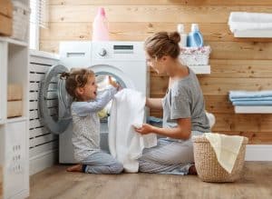 Happy family mother housewife and child daughter in laundry with washing machine