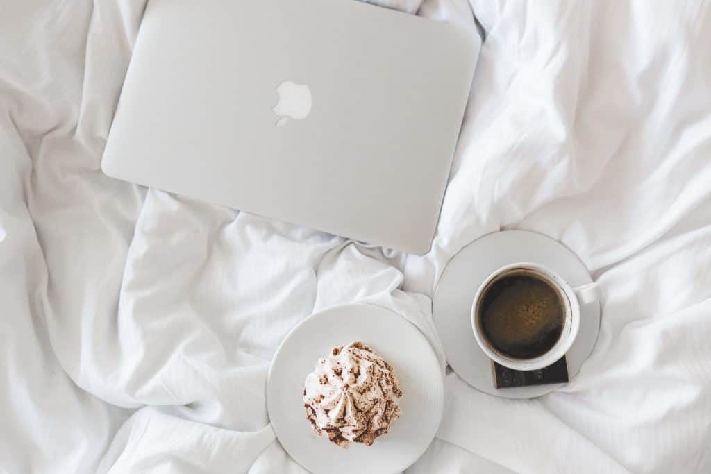 a laptop on a bed with a coffee and muffin