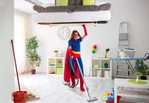 Woman in a superman like outfit holding a couch above her head while vaccuming