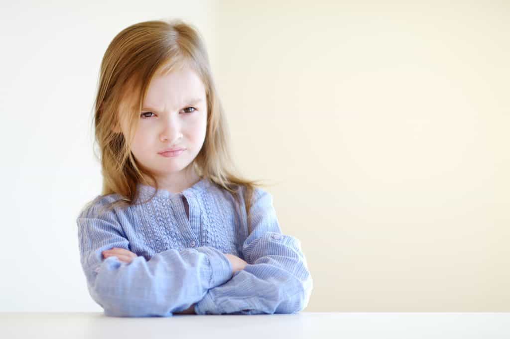 Upset preschool girl withher arms crossed and frowning