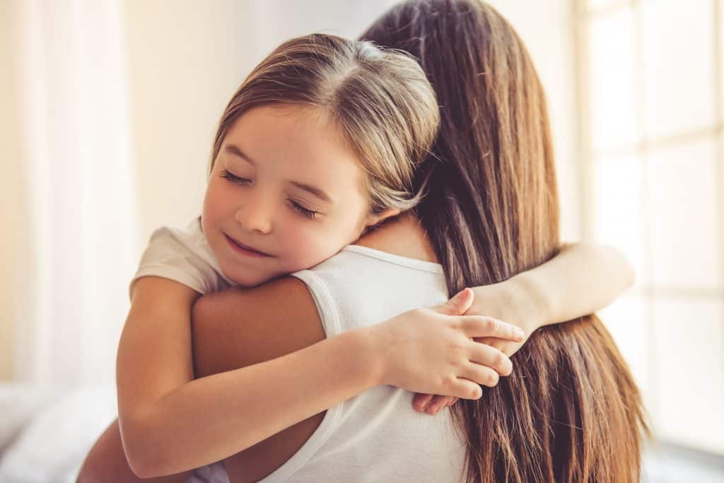 Content girl with her arms around her moms neck hugging her with her eyes closed.