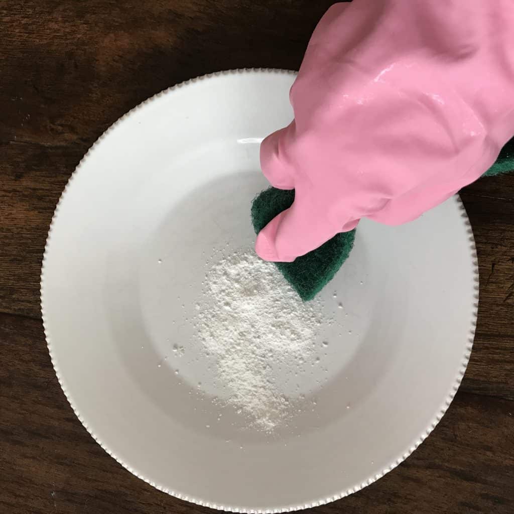 a white plate with a powder cleaner on it and a woman about to scrub it