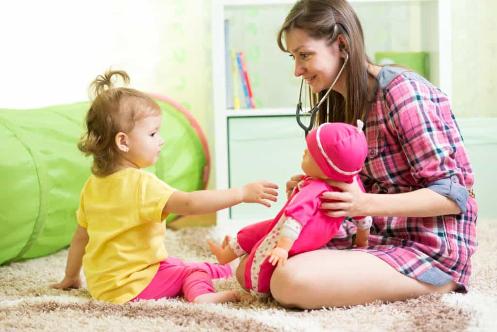 Babysitter playing with a doll with a toddler girl.