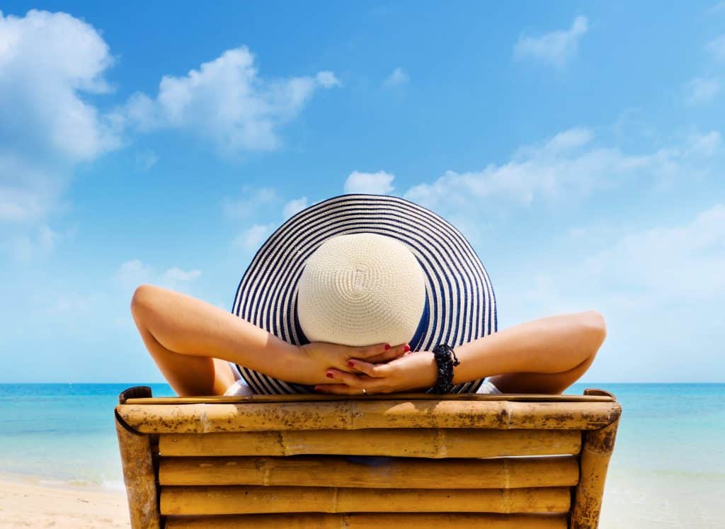 Women living the dream laying out at the beach with her hands behind her head.