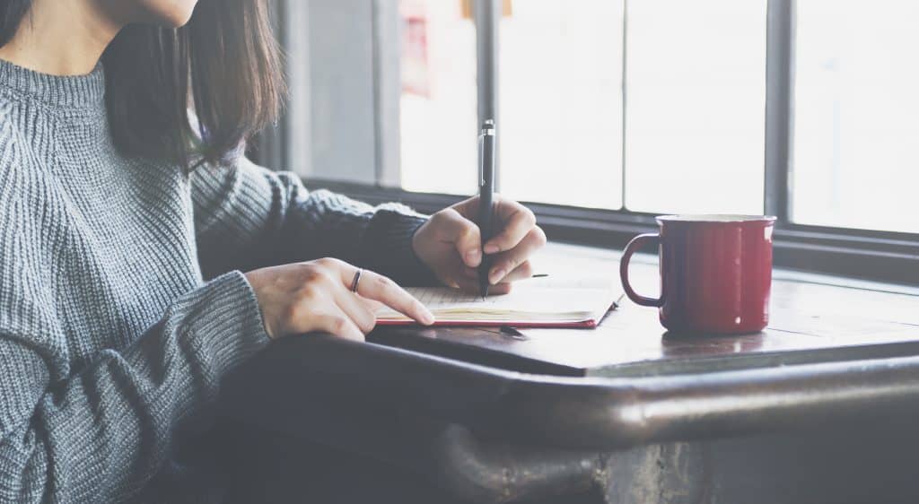 Woman writing in a notebook while having coffee