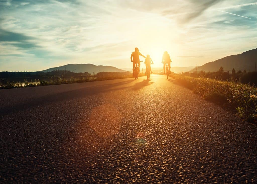 Family of three riding bikes into the sunset.