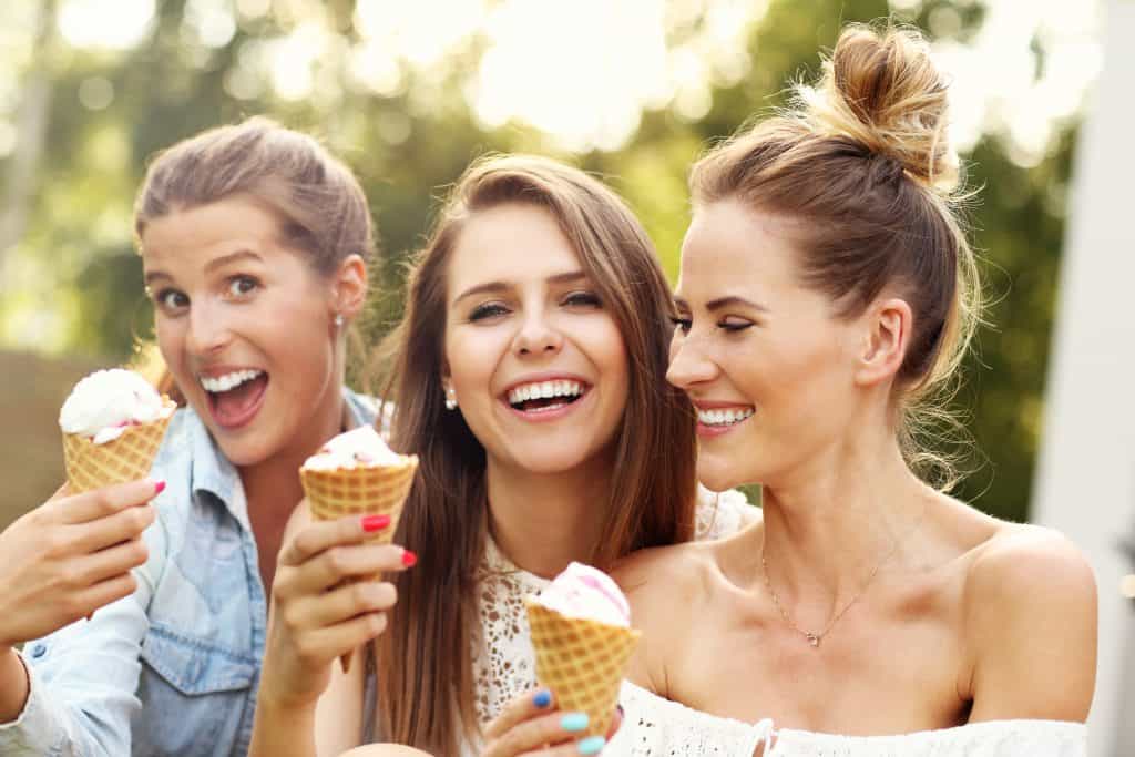 Three pretty ladies having fun eating icecream in a cone.