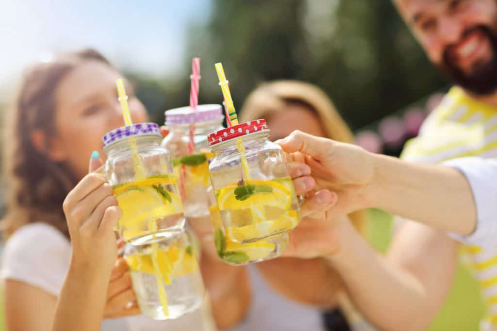 Three adults outside toasting with a glass of lemon water