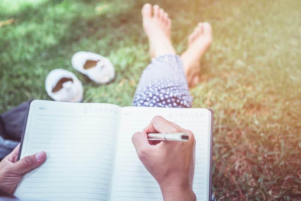 Women reflecting, writing in a journal, outside.