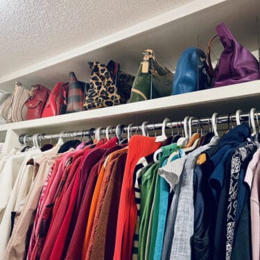 hand bags organized in color order on the top shelf with a rack of clothes also organized in color order below. Two helpful ideas to organize closets.