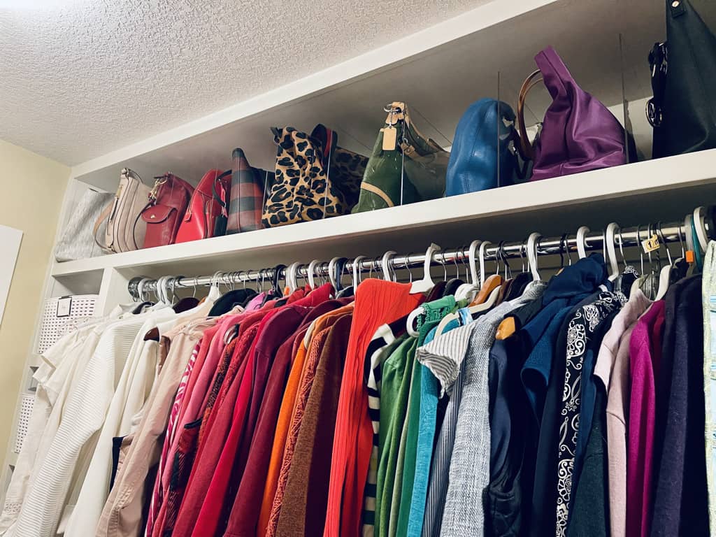 handbags on the top shelf arranged by color and clothes on the second level arraged by color int he organized closet.