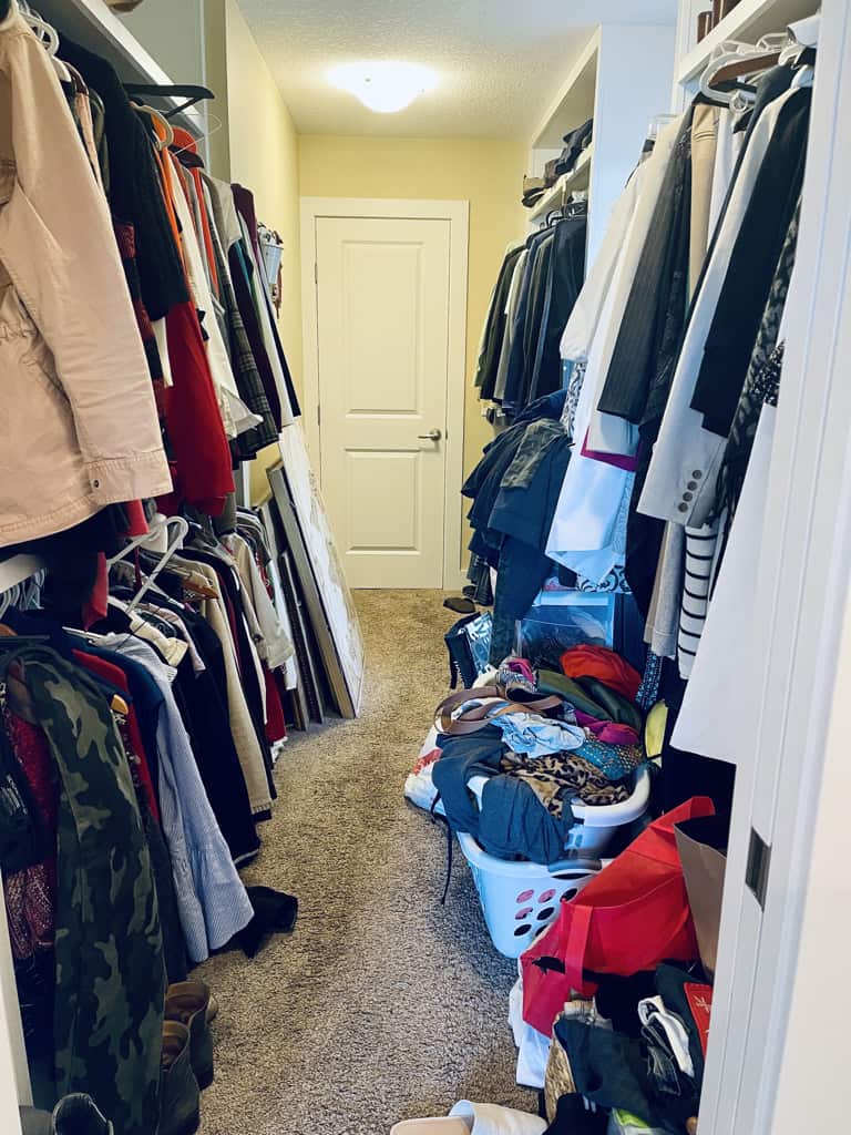 Messy cluttered closet with bins on the floor and clcothes all over the place.