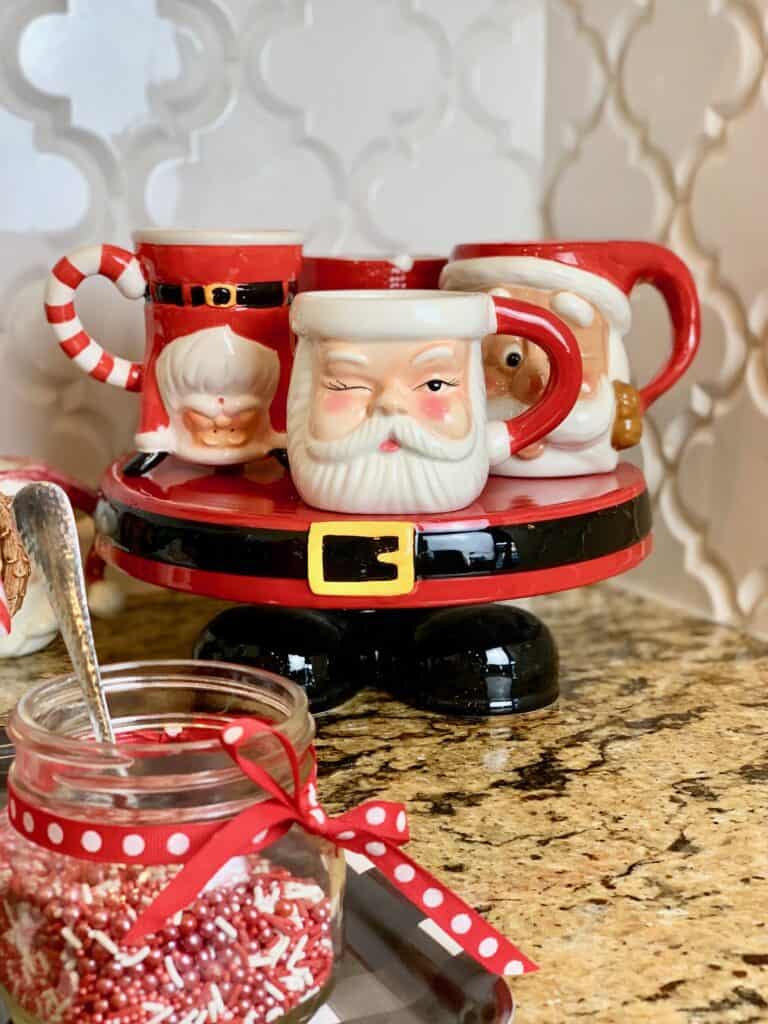 Santa coffee cups on a platter with sprinkles as a topping in a jar.