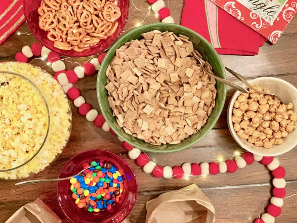 top view of mixins for a diy party mix including popcorn, pretzals, chex cereal, carmel popcorn, and M&Ms