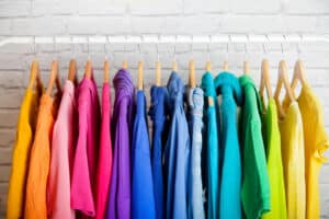 Rainbow clorored shirts hanging displaying The HOme Edit's Home Organization style.