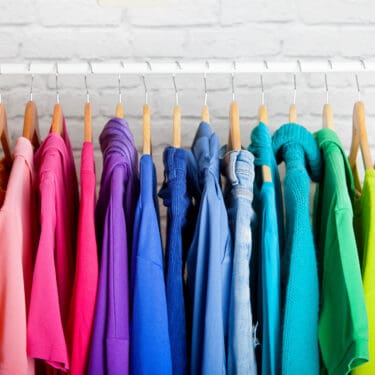 Rainbow clorored shirts hanging displaying The HOme Edit's Home Organization style.