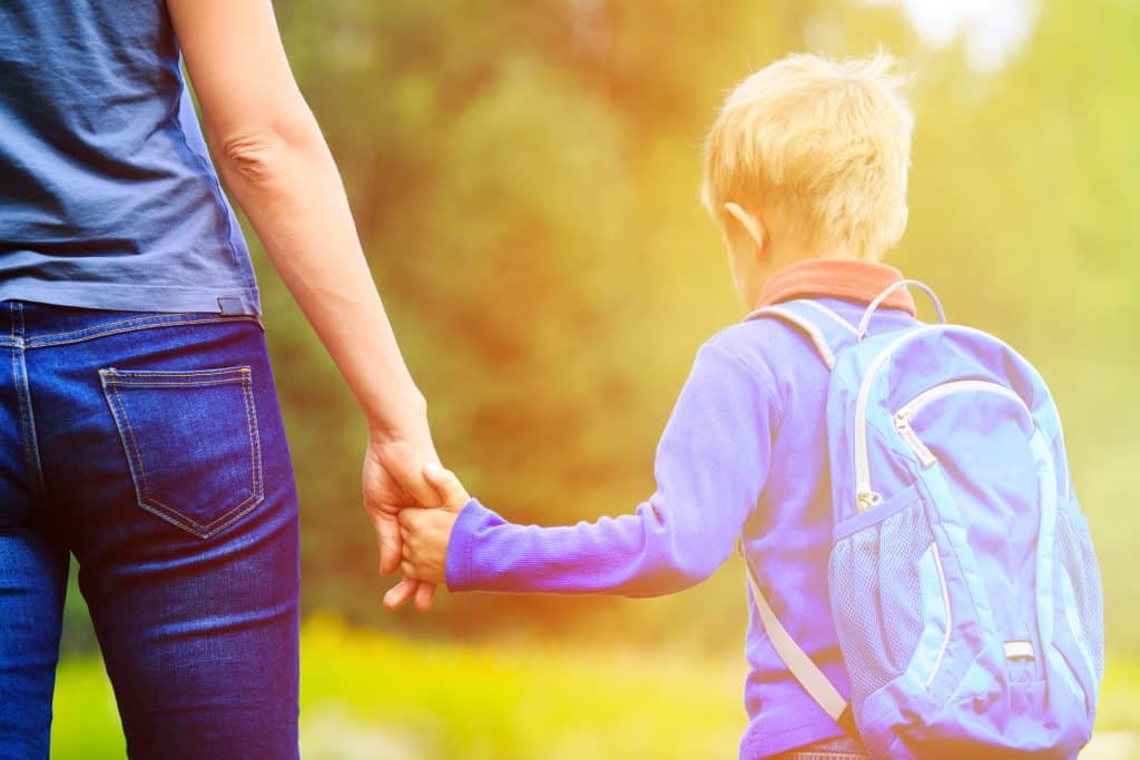 Mom holding child's hand taking him to the first day of school