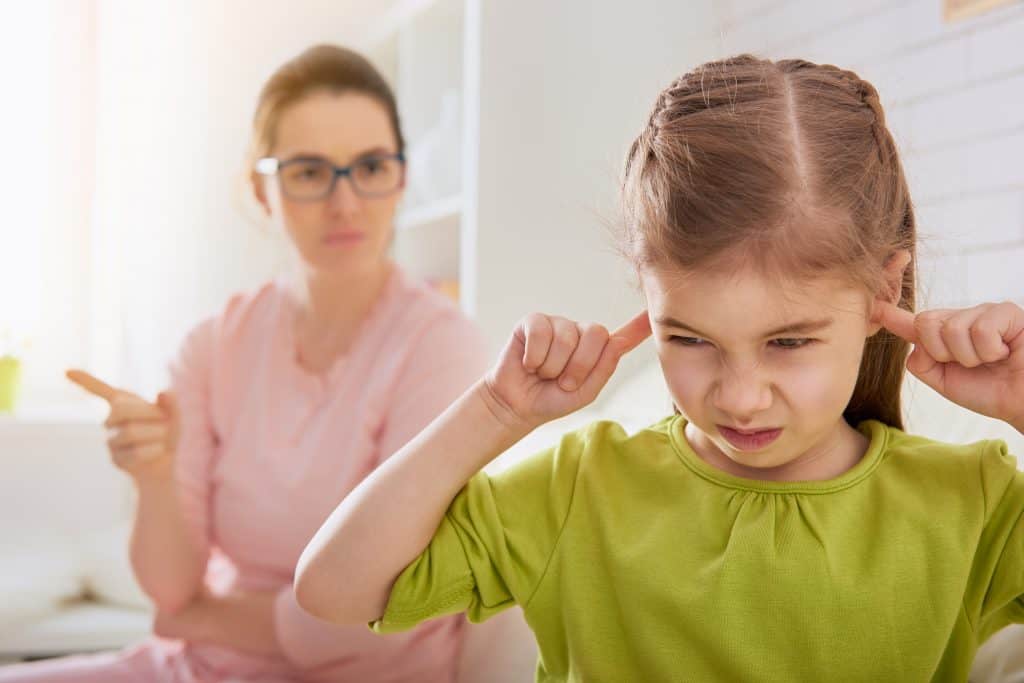 Mom upset and looking at her daughter, young daughter plugging her ears