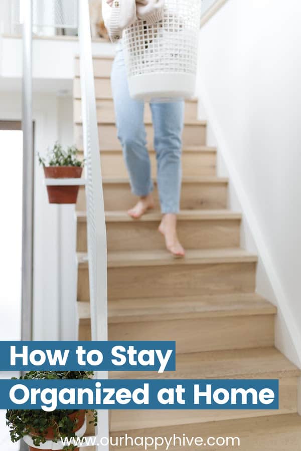 Picture of a woman walking down stairs carrying laundry with post title How to Stay Organized at Home