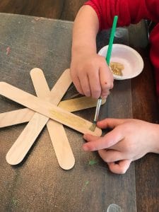 child decorating popsicle stick snowflake