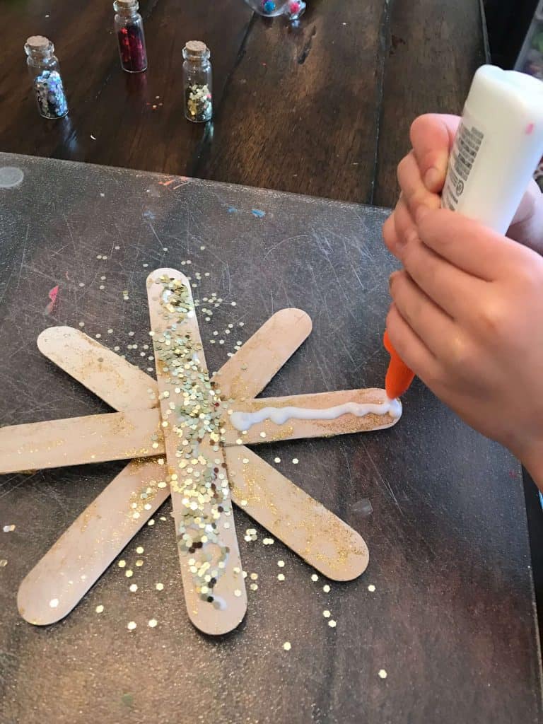 child decorating popsicle stick snowflake