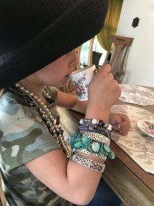 Preschooler dressed up in a broad brimmed hat with lots of jewelry on while sipping tea.