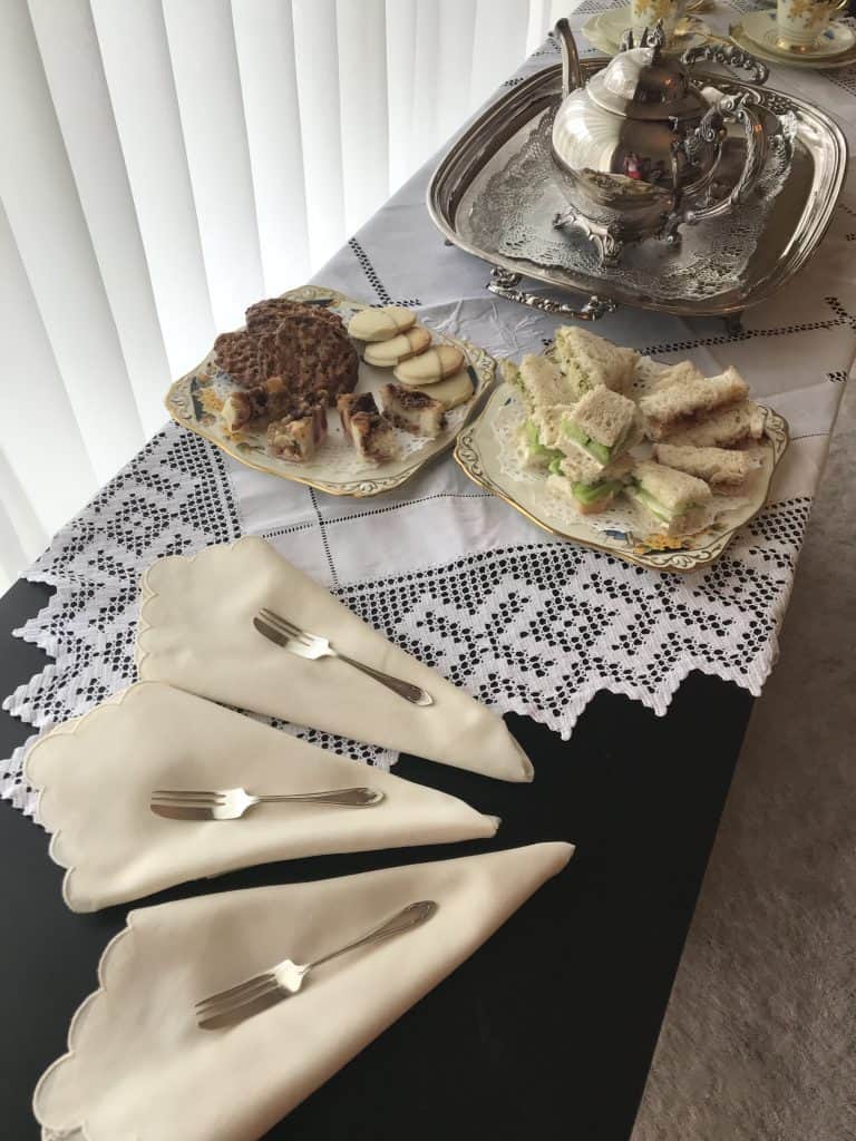 Tea sandwhiches and desserts next to a silver tea set.