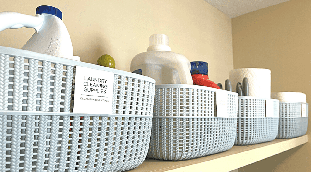 a row of four blue bins that are organizing the laundry cleaning supplies, detergens, lint rollers, and paper towels. The bins have labels from amazon that help with home organization.