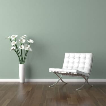 white modern chair and a vase of calla lilies on a pale green wall