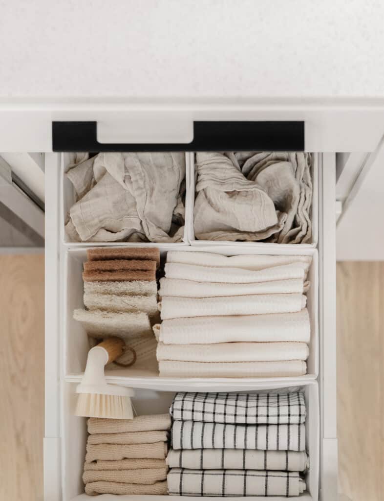 Light-colored dishcloths folded in small rectangles and vertically filed in a drawer to help with home organization.