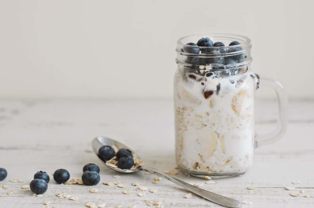 Overnight oats with whole grain cereal, fresh bluberries and coconut milk served with a spoon on wooden table. Healthy dessert for breakfast