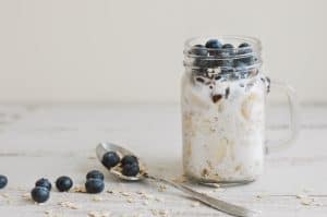 Overnight oats with whole grain cereal, fresh bluberries and coconut milk served with a spoon on wooden table. Healthy dessert for breakfast