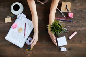 Woman sorting out mess on working table, moving stationery, documents, food and plant