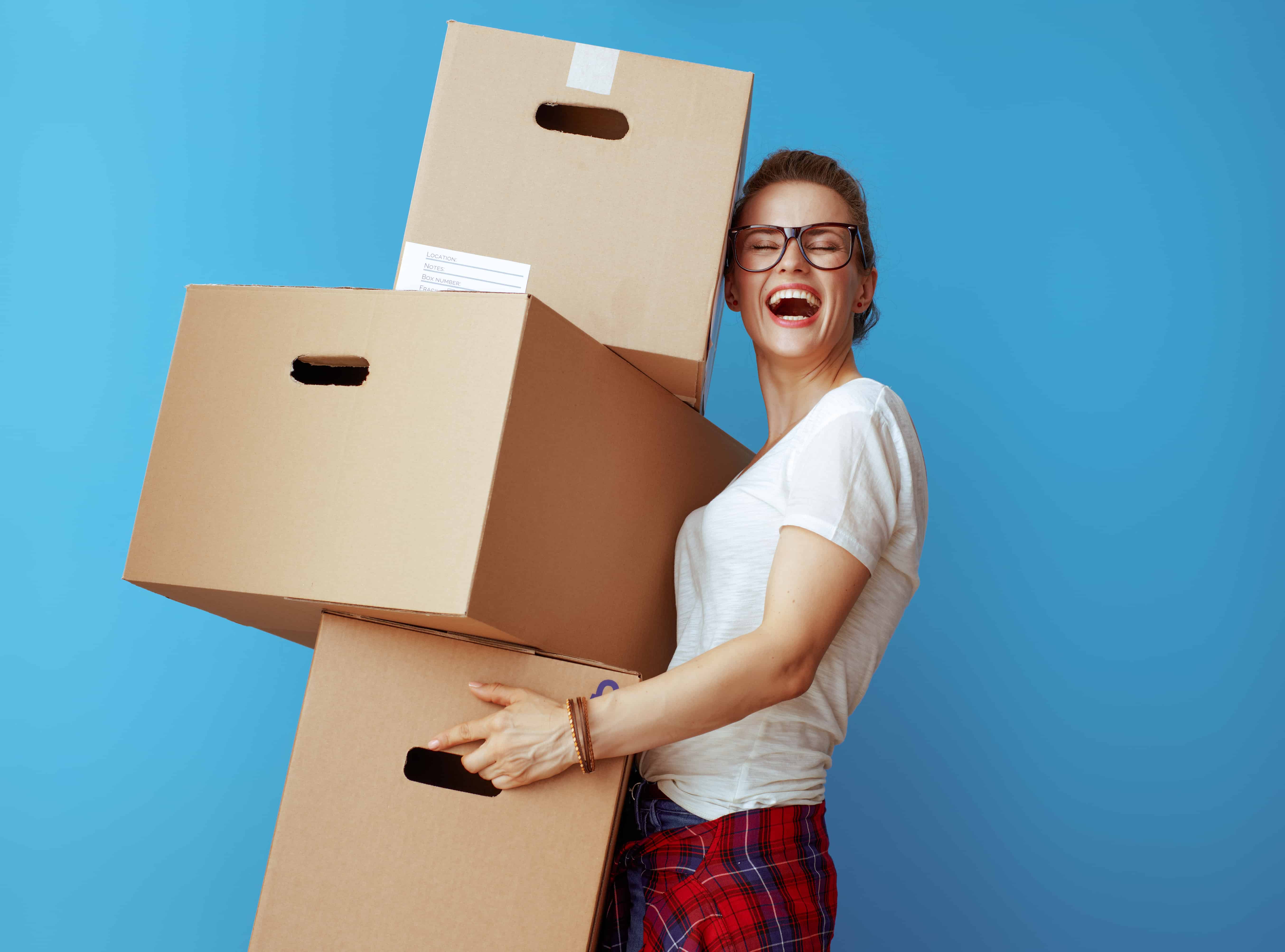 Woman holding boxes and smiling after decluttering and preparing for a move.