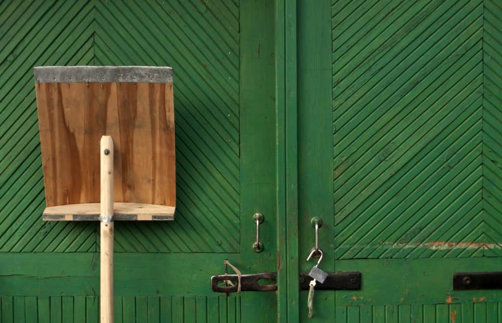 Wooden snow shovel in fron of green hangar door. Tools.