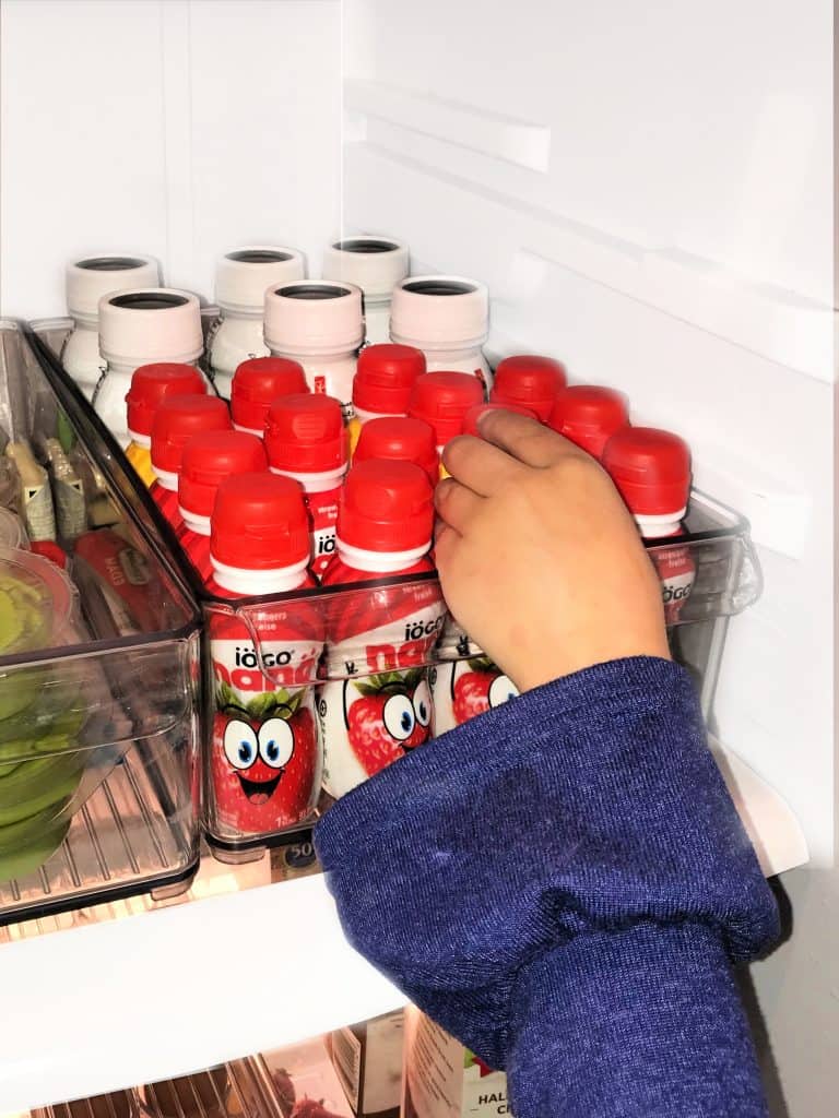 Young girls hand reaching to grab a yogurt drink from a clear plastic container