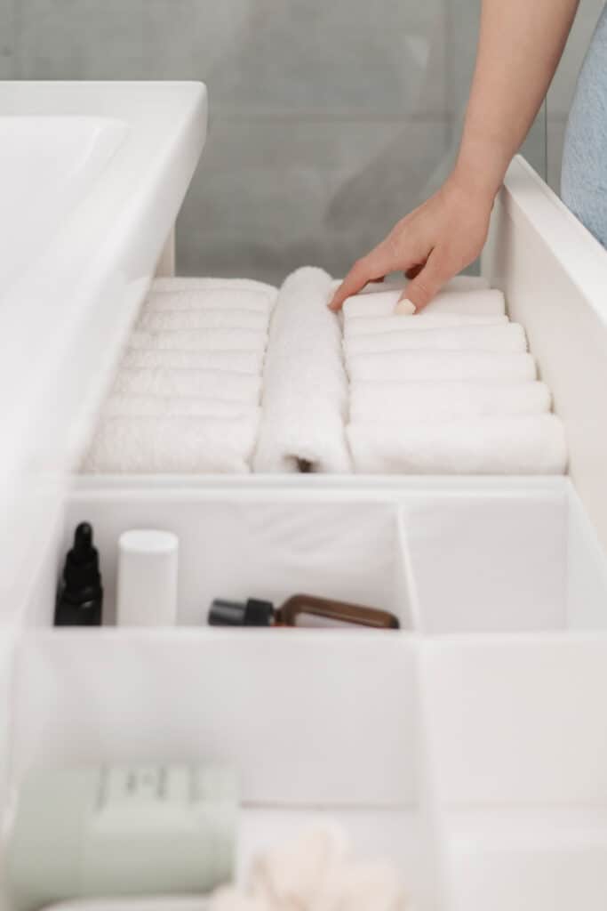Picture of white washcloths folded in small rectangles and vertically filed in a drawer to help with home organization.